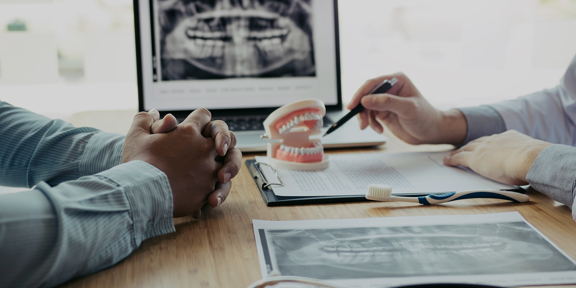 Dentist pointing at denture model with X-rays in background.