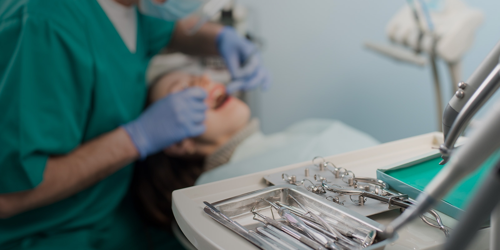A table with dental tools in focus while a dentist works in the blurred background.