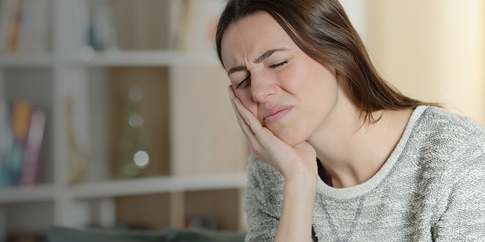 A woman holding her cheek, appearing to be in pain.