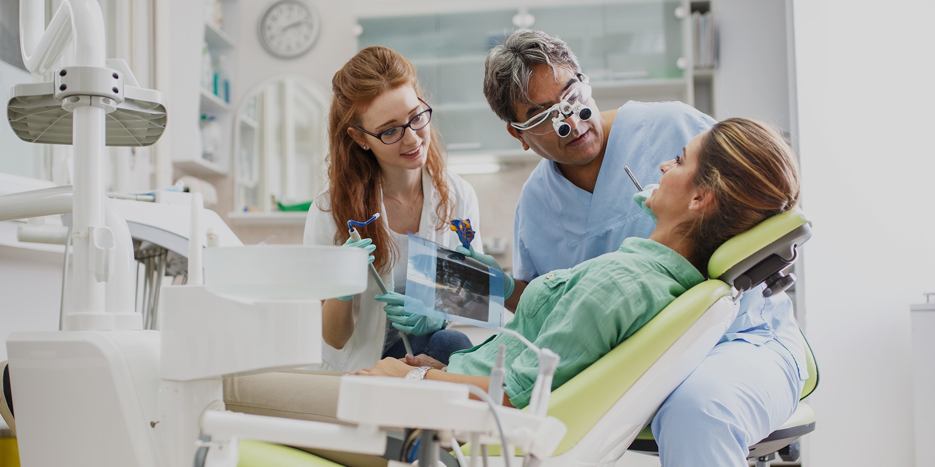 A dentist and dental assistant looking at a patient seated in the dental chair.