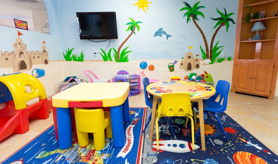 Colorful kids’ playroom with two bright tables, small chairs, toys, and a TV on the wall.