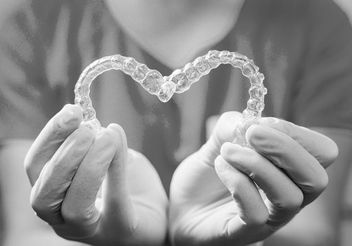 A doctor holding two clear aligners shaped into a heart.