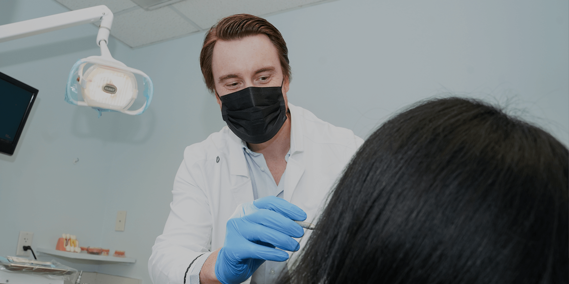 A dentist wearing a black mask working on a patient.