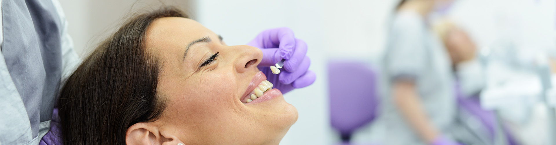 dentist holding tooth shade-matching tool against woman's teeth